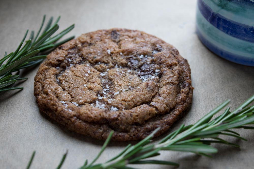 brown butter chocolate chip cookie on parchment paper with rosemary sprigs