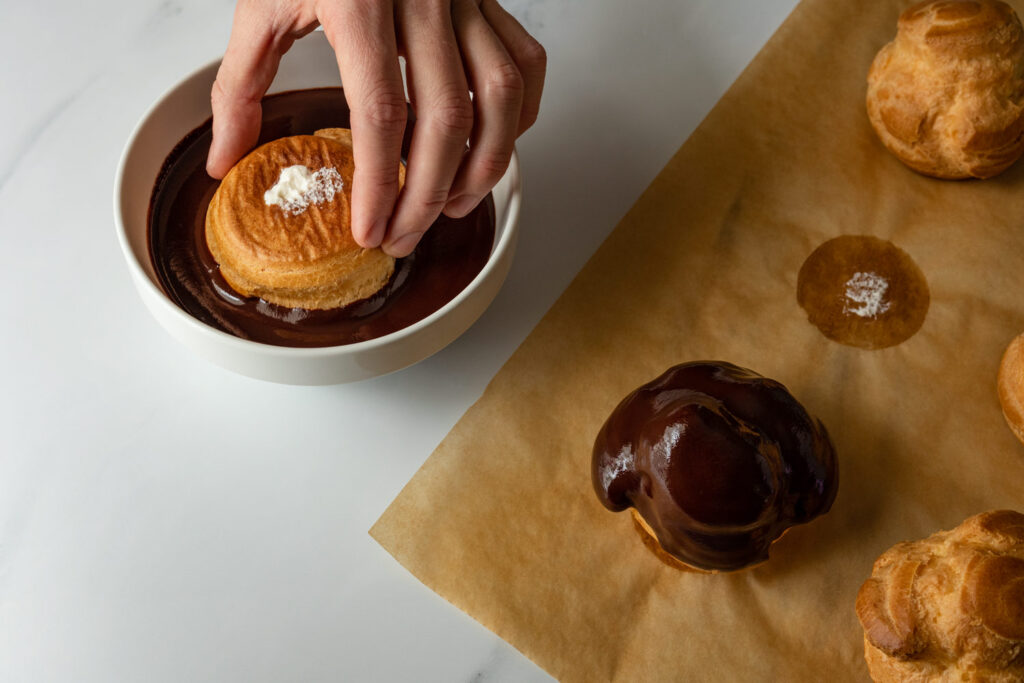 dipping the bossche bollen in a bowl filled with chocolate glaze