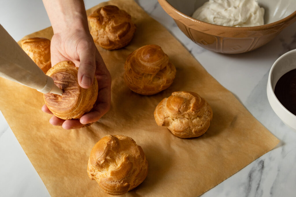 using a piping bag to fill the choux pastries with whipped cream