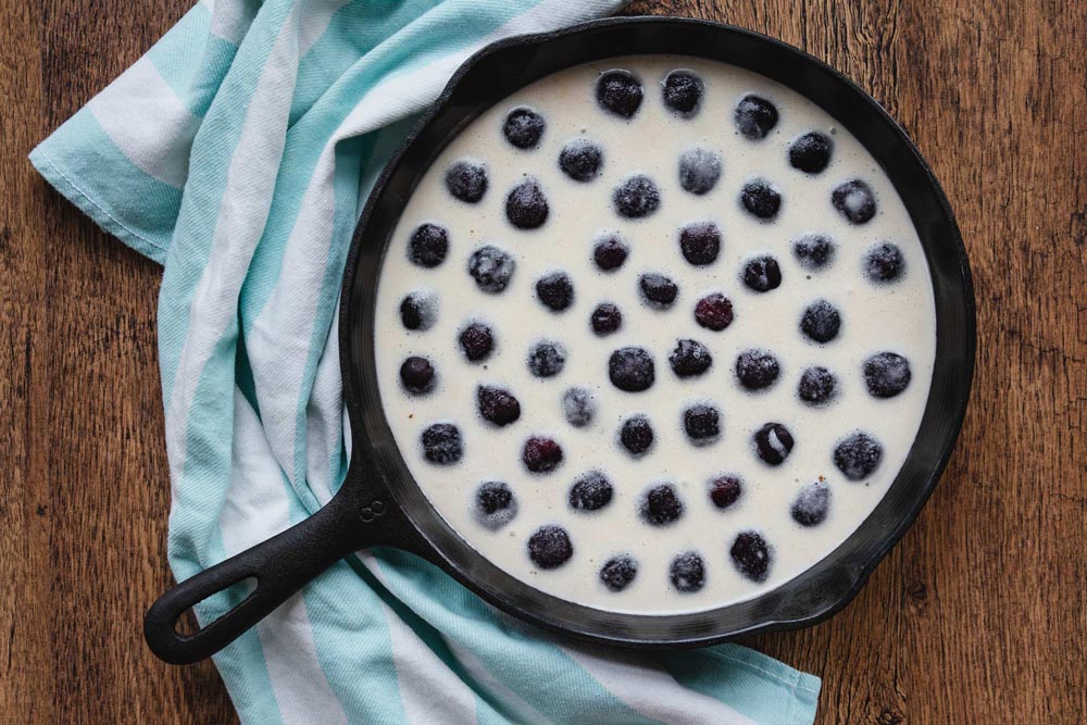 cherries and clafoutis batter in a cast iron skillet