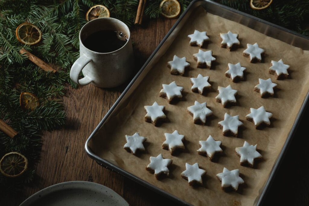 baking tray of zimtsterne cinnamon star cookies with garland and a mug of coffee