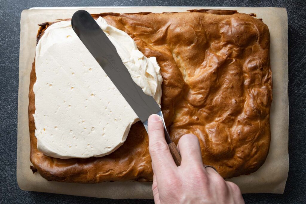 spreading the krem filling onto the pastry with an offset spatula