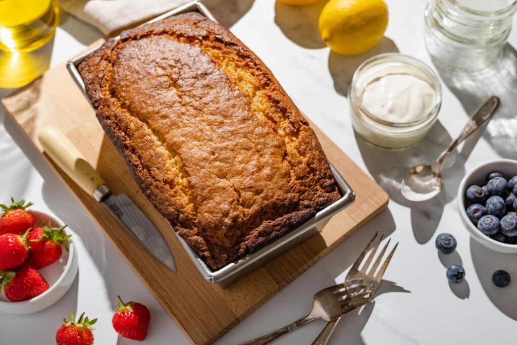french yogurt loaf cake with strawberries, blueberries, yogurt pot, lemons, and silverware