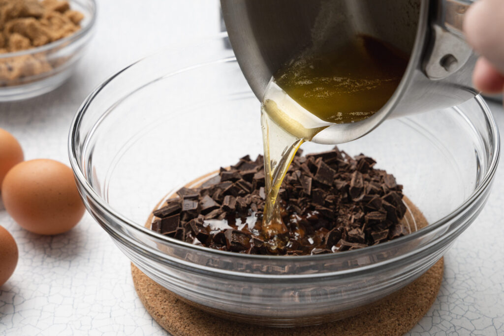 pouring melted butter into a glass bowl with chopped chocolate
