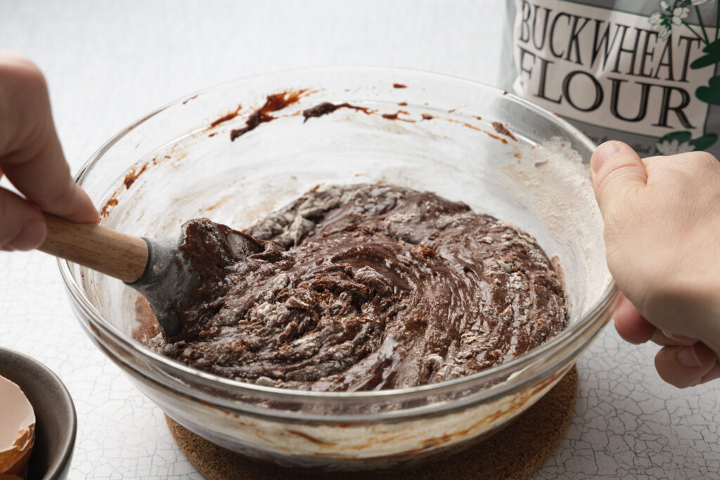 hands stirring chocolate cookie dough in a glass mixing bowl