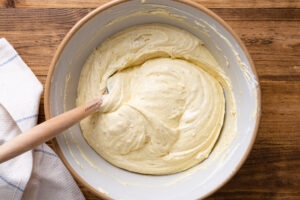 Smooth, pale pound cake batter in a large ceramic bowl with a spatula, ready to pour into the pan
