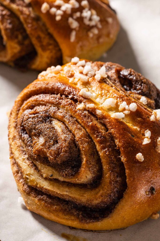 A closeup of baked korvapuusti cinnamon buns on a baking sheet lined with parchment paper