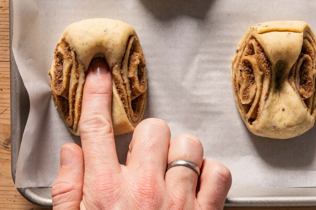 An overhead photo of a finger pressing into a cinnamon bun to create a dimple