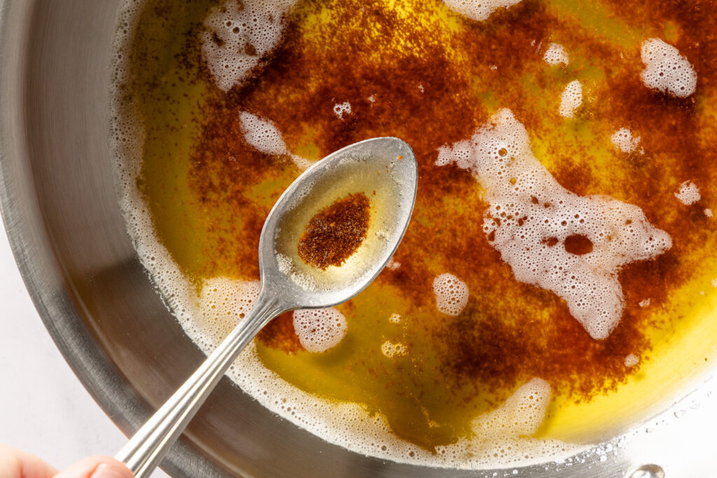 Brown butter in a spoon over a light-colored sauté pan
